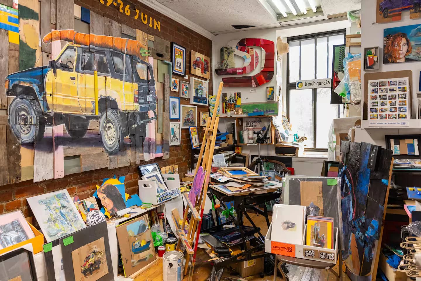 Artist studio filled with canvases, an easel and a large truck painting, from an artist represented by L'Original